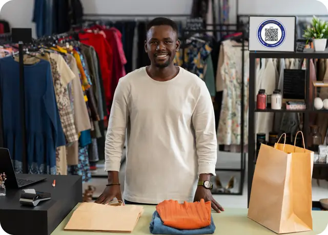 Un commerçant souriant dans sa boutique de prêt-à-porter, derrière son comptoir